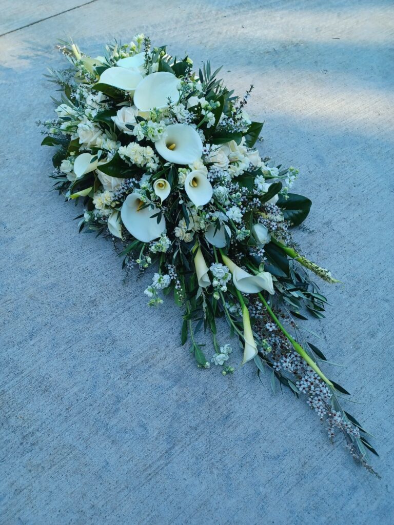 Kin Florist casket spray featuring a mix of white flowers, roses, lillies, and various foliage, for a Warkworth church funeral service.