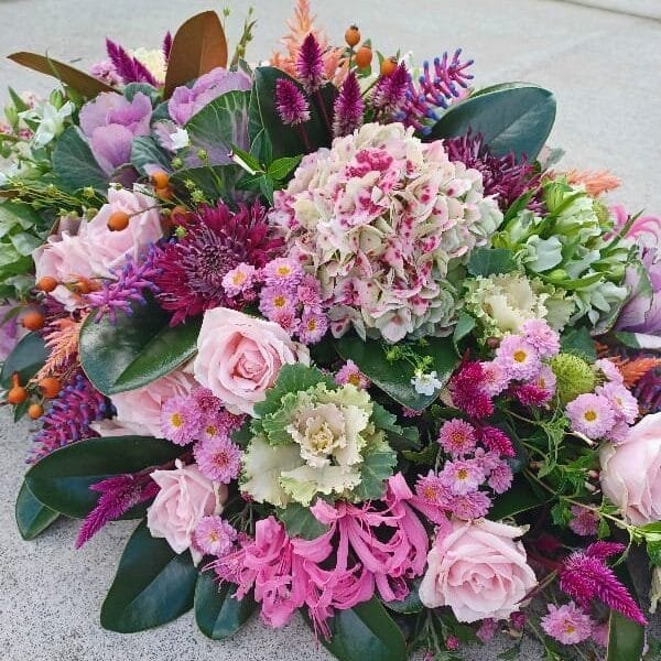 Detail shot of a Kin Florist casket spray delivered to Jason Morrison Funerals for a Warkworth service. It uses seasonal, local flowers in pinks, purples, whites and oranges,  including roses, nerines, celosias, and ornamental kale. 