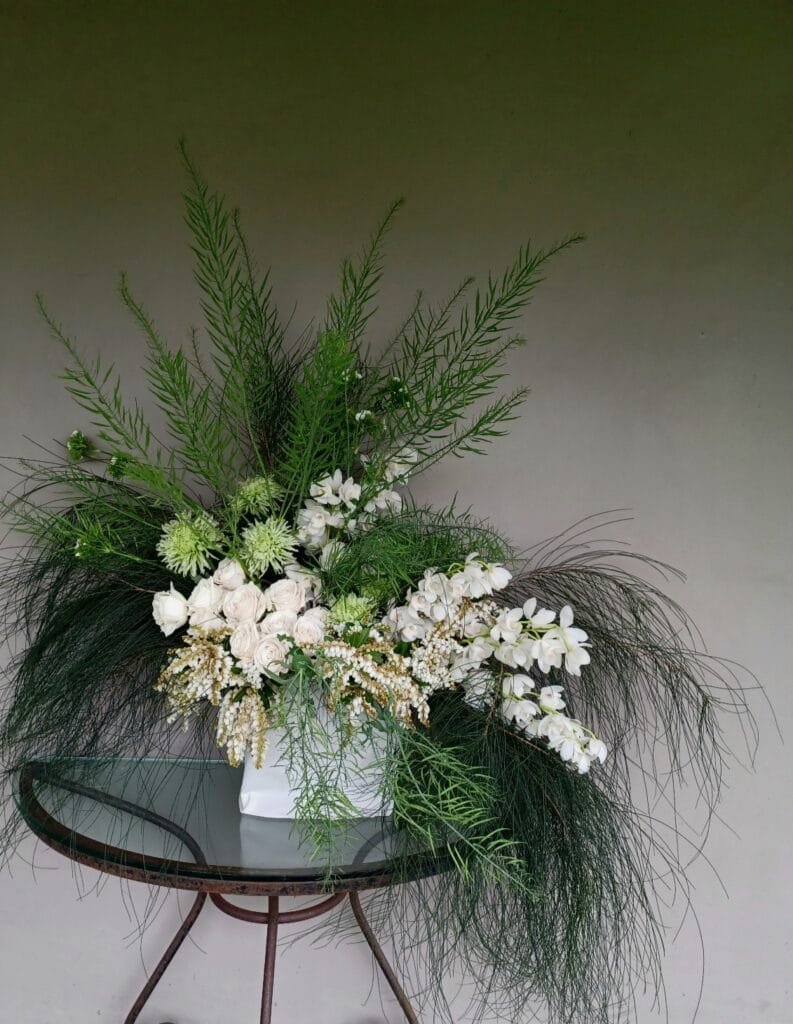 Kin Florist wedding flower arrangement in Matakana. The luxurious statement arrangement features white roses and orchids, and graceful flowing foliage. It has a modern, romantic garden vibe.