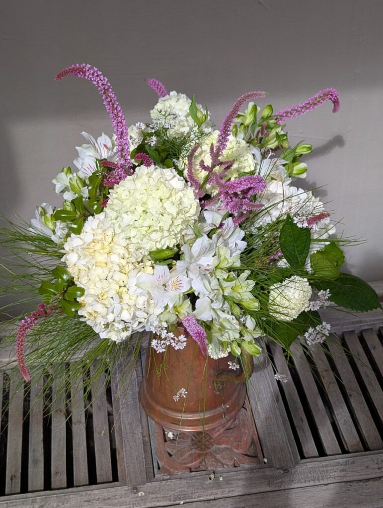Seasonal garden style floral table arrangement by Kin Florist Matakana. Fluffy white snowballs, alstroemeria, delicate accent flowers, and textural greenery.